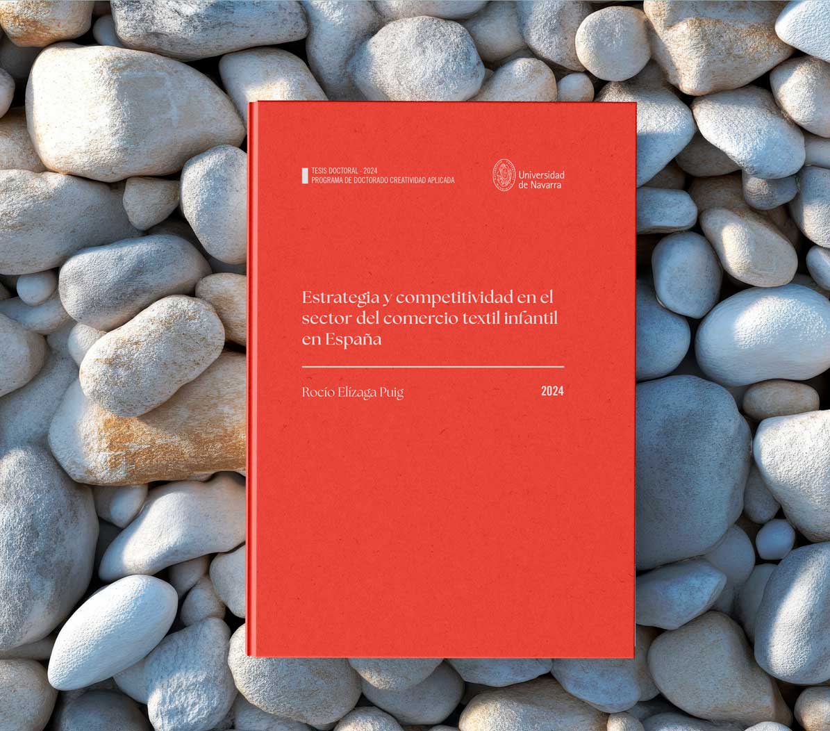 Ejemplo de maquetación de tesis doctoral Estrategia y competitividad en el sector infantil en España de Rocío Elizaga Puig. Universidad de Navarra. La cubierta es roja con letras blancas sobre un fondo de piedras de playa grandes